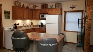 A kitchen with wooden cabinets, a white refrigerator, a microwave, a stove, and two black chairs labeled "Ranger".