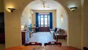 Un comedor con una mesa y sillas de madera, un cuenco decorativo y vistas a un salón con sofá y mesa de centro a través de un arco.