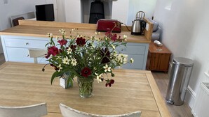 A kitchen with a wooden table, two white chairs, a vase of flowers, a red toaster, and a kettle. - Crugsillick Studio -  a barn conversion that sleeps 4 guests  in 2 bedrooms (Ruan high Lanes)