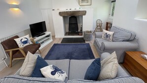 A cozy living room with a fireplace, striped sofas, a television, and a bookshelf. - Crugsillick Studio -  a barn conversion that sleeps 4 guests  in 2 bedrooms (Ruan high Lanes)
