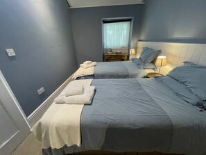 Een slaapkamer met twee bedden, een nachtkastje, een lamp en een raam met gordijnen.