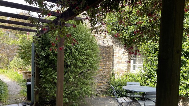 Un patio de piedra con una pérgola, un muro de piedra y una mesa con bancos.