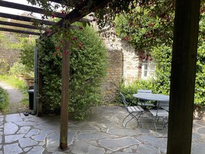 Een terras van natuursteen met een pergola, een stenen muur en een tafel met bankjes.
