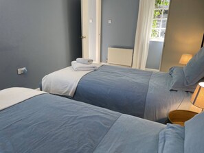 Een slaapkamer met twee bedden, een radiator, een raam met gordijnen en een bedlampje.