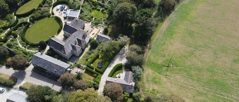 Luchtbeeld van een groot landgoed met meerdere gebouwen, aangelegde tuinen en een uitgestrekt veld.
