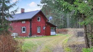 Une maison en bois rouge avec un toit en métal, une antenne parabolique et une porte de garage blanche.