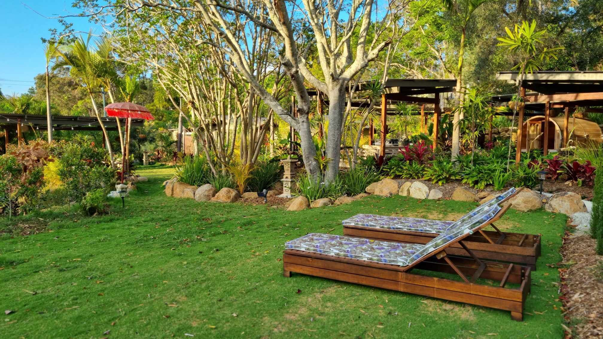 A garden with two wooden lounge chairs, a red umbrella, and a stone lantern.