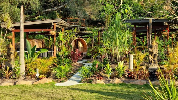 Un jardín con un porche de madera, una estructura de madera circular y una estatua.