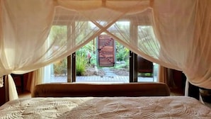 Un dormitorio con cama con dosel, y vistas a una terraza de madera y jardín a través de amplios ventanales.