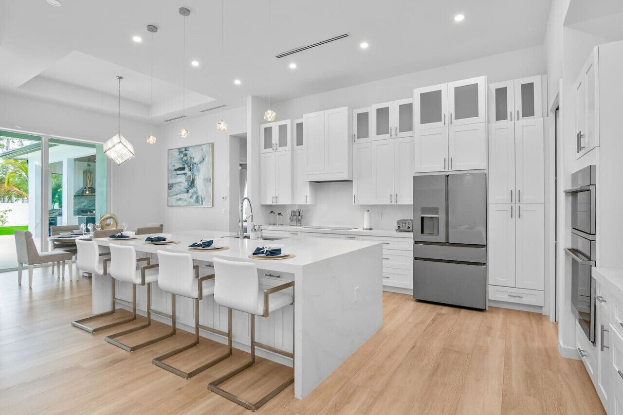 A modern kitchen with white cabinetry, a central island with bar stools, stainless steel appliances, and pendant lighting.
