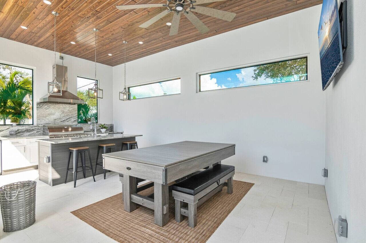 A modern kitchen with a marble countertop, wooden ceiling, and large windows.