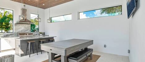 A modern kitchen with a marble countertop, wooden ceiling, and large windows.