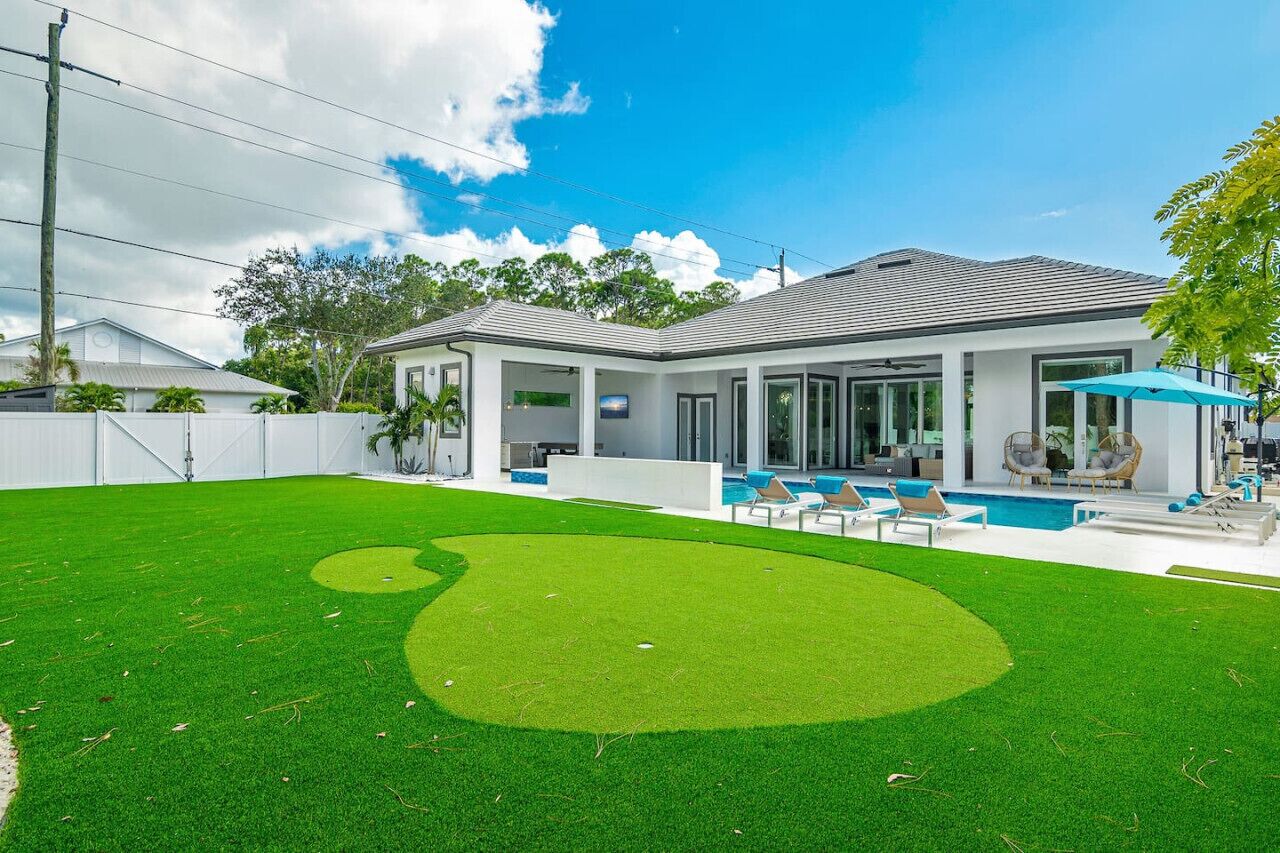 A modern house with a swimming pool, a covered patio, and a well-maintained lawn.