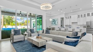 A modern living room with a large sofa, coffee table, and a view of a swimming pool. - Blue Diamond Beach Home (Bonita Springs)