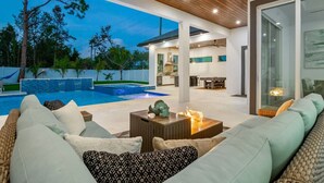 A modern outdoor living area with a pool, comfortable seating, and a view of the surrounding landscape. - Blue Diamond Beach Home (Bonita Springs)