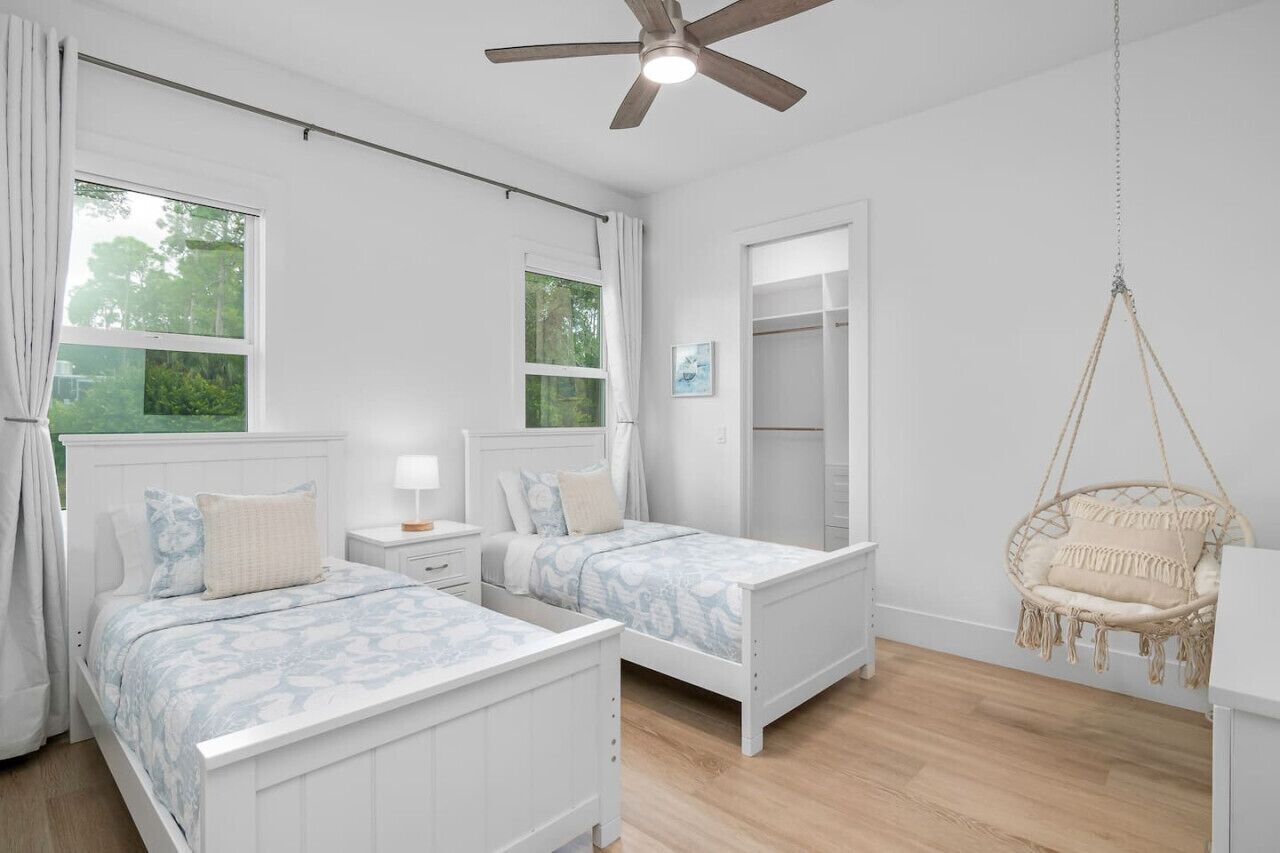 Une chambre avec deux lits, un fauteuil suspendu, une armoire et un ventilateur de plafond.