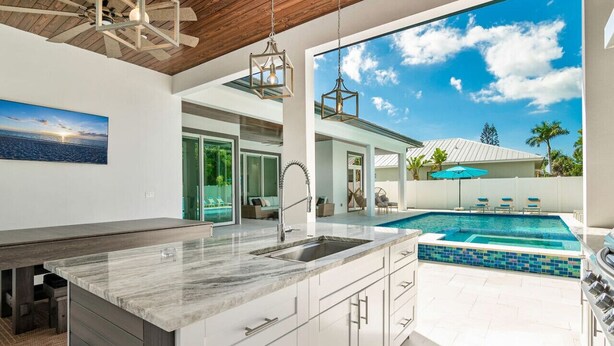 A modern kitchen with a large island, a built-in sink, and a view of a swimming pool. - Blue Diamond Beach Home (Bonita Springs)