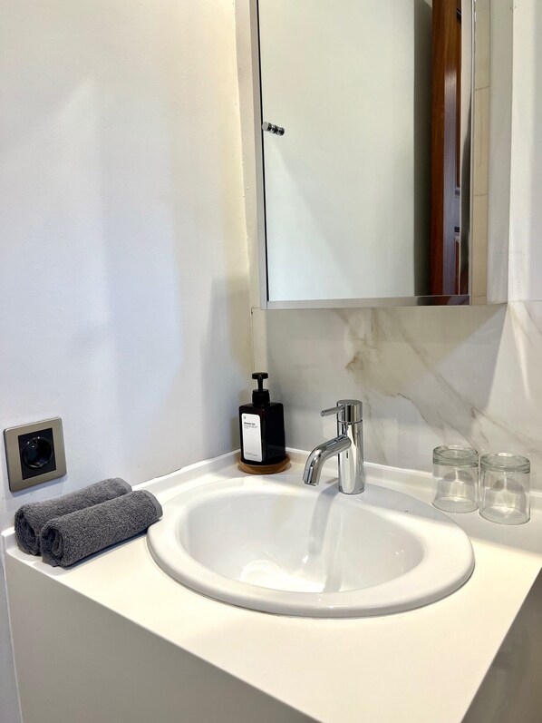 A bathroom with a white sink, a mirror, a soap dispenser, and two towels. - Charlie Guest House (Nusa Dua)