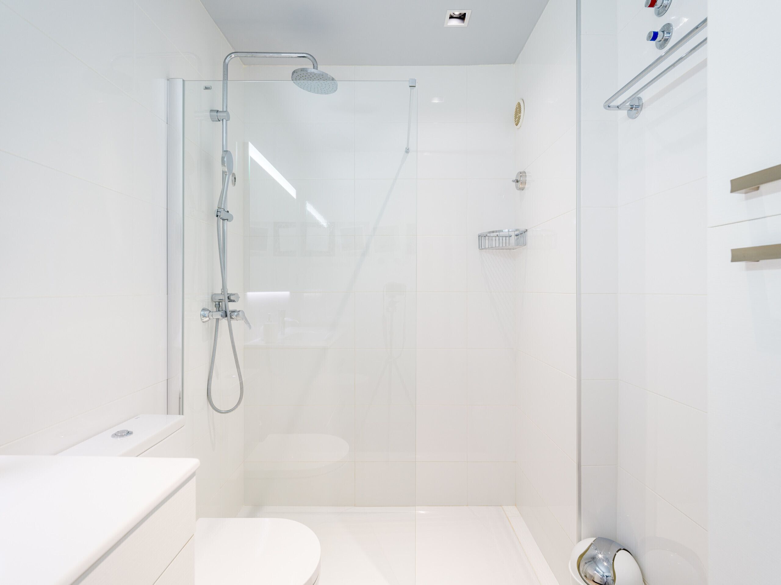 Un bany modern amb dutxa de vidre, un vàter blanc i un lavabo.