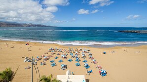A beach with numerous sun loungers and umbrellas, a clear sky, and the ocean in the background.
