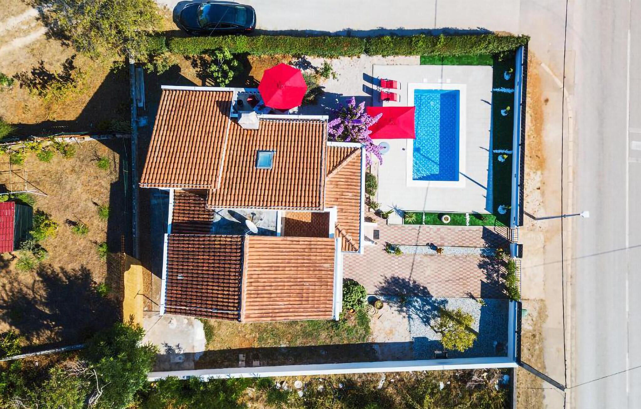 An aerial view of a property with a swimming pool, a red umbrella, and a tiled roof.