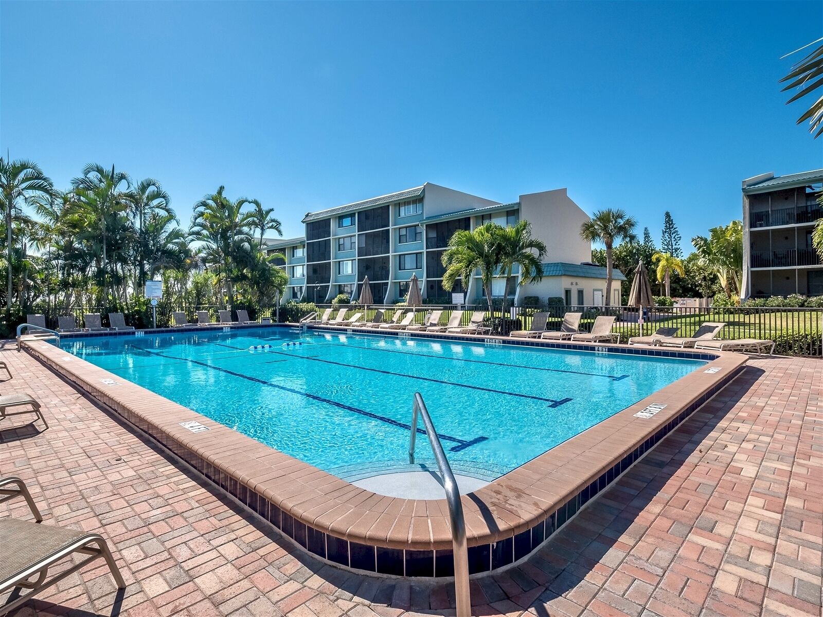 Uma piscina retangular com água azul cristalina, rodeada por espreguiçadeiras e um deck de tijolos.
