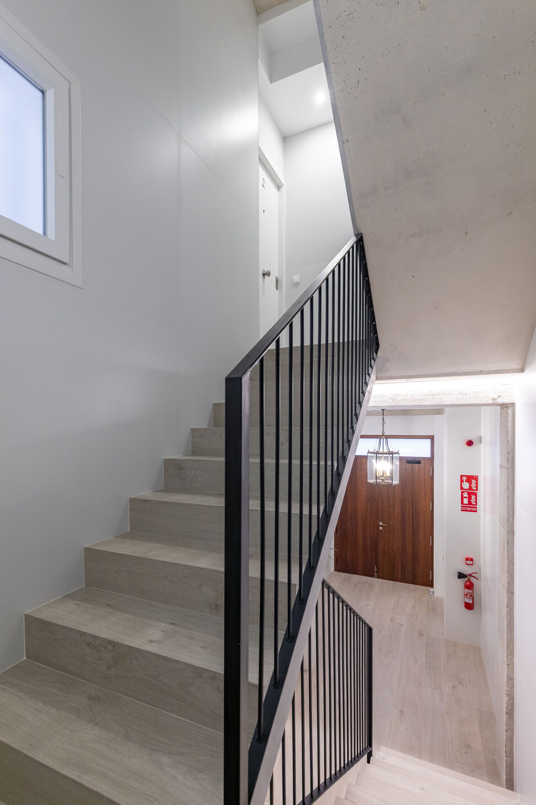 A staircase with wooden steps and black metal railings, leading to a room with a wooden door and a fire extinguisher on the wall.
