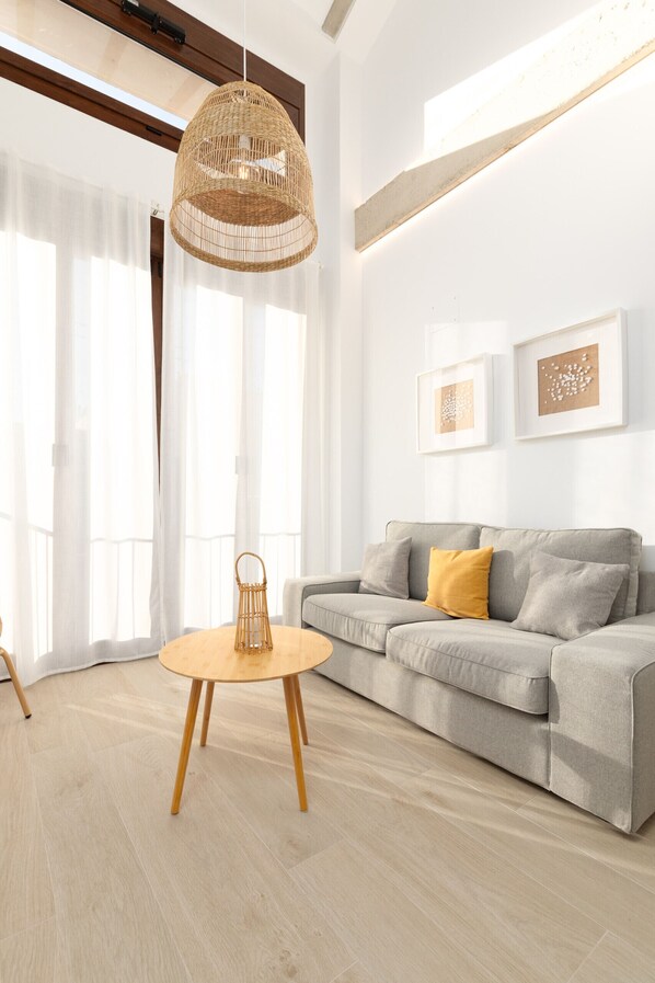Un salon moderne avec un canapé gris, une table ronde en bois et un luminaire suspendu en fibres tressées.