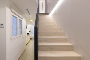 Eine moderne Treppe mit Holzdielen und einem schwarzen Geländer, die zu einer Zwischenebene mit einer Leuchte führt.