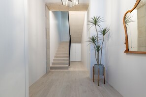 Un couloir étroit avec un escalier menant à l’étage supérieur, un grand miroir sur la droite et deux plantes en pot.