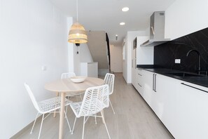 Moderni keittiö, jossa on valkoiset kaapit, musta työtaso ja pyöreä ruokapöytä valkoisine tuoleineen.