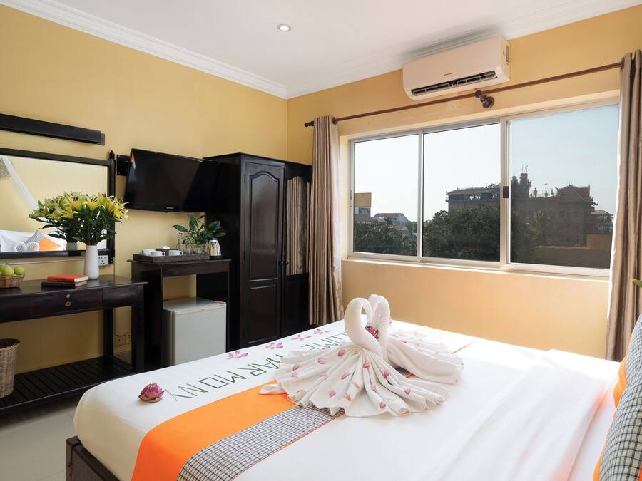 Habitación de hotel con cama, escritorio, televisor y ventana con vista a edificios.