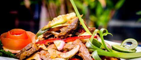 Un plato de carne salteada con verduras y una rodaja de lima.