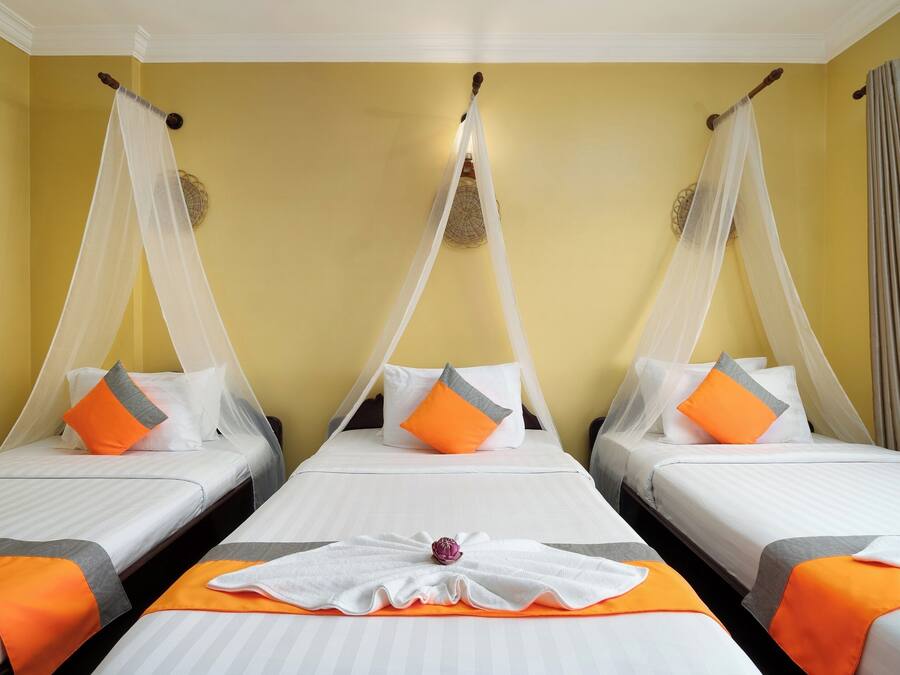 Een hotelkamer met drie bedden, elk met een hemelbed en oranje kussens.