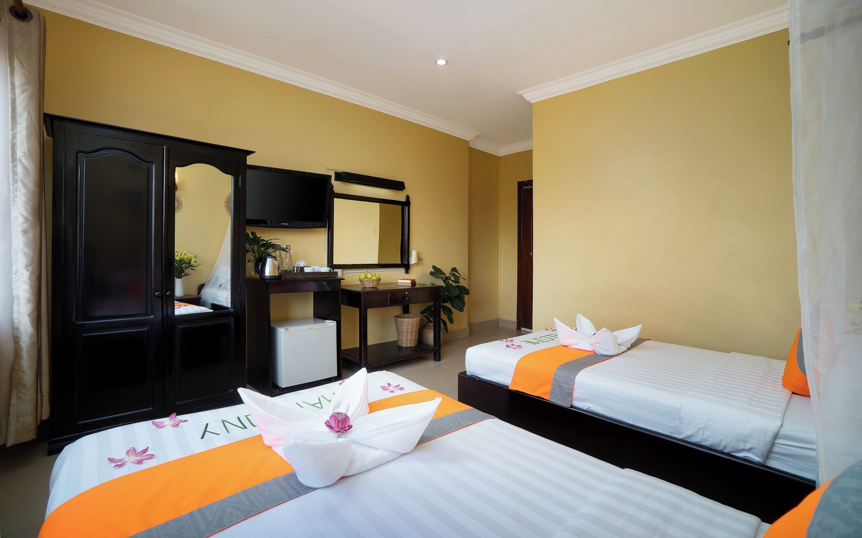 A hotel room with two beds, a desk with a computer, a television, and a mirror.