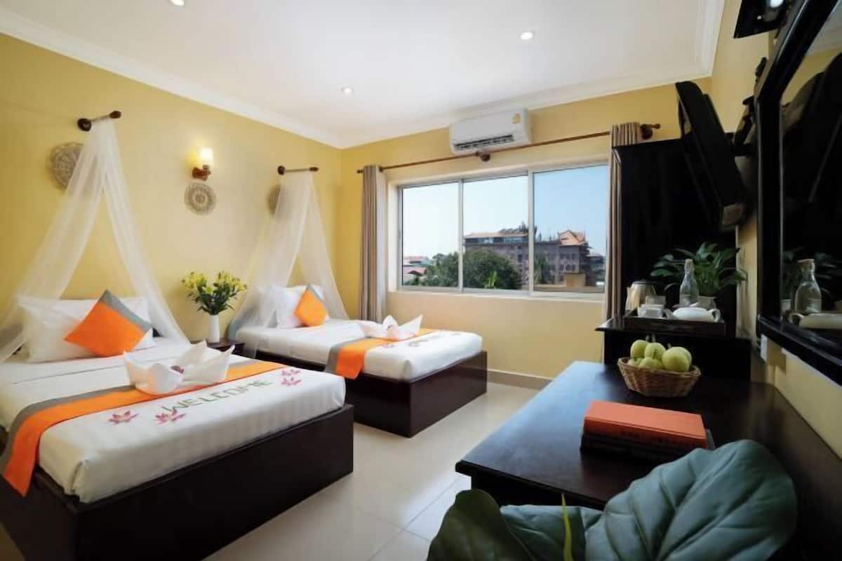 Ein Hotelzimmer mit zwei Betten, einem Fenster mit Aussicht, einem kleinen Tisch mit einer Obstkorb und einem Fernseher an der Wand.