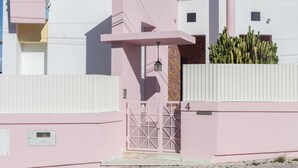 A pink building with a gated entrance, a small balcony, and a cactus plant. - FLH Caparica Town House with Pool (Charneca de Caparica)