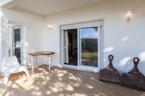 Une terrasse avec une chaise en plastique blanche, une petite table ronde et deux jardinières en osier.