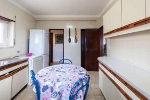 Eine kleine Küche mit weißen Schränken, einem weißen Kühlschrank, einer Holz Arbeitsplatte und einem Tisch mit einer blumigen Tischdecke.