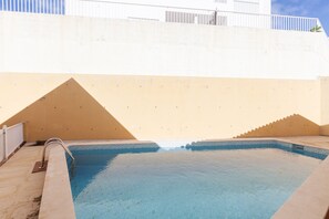 Une piscine dotée d’une barrière blanche, d’une petite cascade décorative et d’un mur beige orné d’un motif géométrique.
