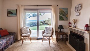 Un salon comprenant un canapé, deux fauteuils, une cheminée et une vue sur l’extérieur, visible à travers une porte vitrée.