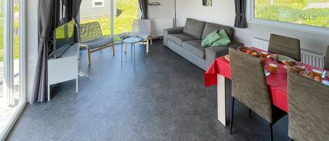 Ein modernes Wohnzimmer mit einer Couch, einem Esstisch, der für das Frühstück gedeckt ist, und einem großen Fenster mit Vorhängen.