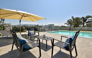 An outdoor pool area with lounge chairs, a table, and an umbrella.