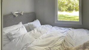 A bedroom with a bed, white bedding, a headboard, a window with a view of greenery, and a white device on the wall. - Beautiful home in Färjestaden with WiFi (Färjestaden)