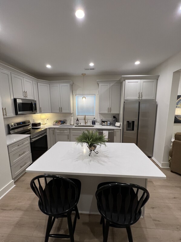A modern kitchen with white cabinets, stainless steel appliances, and a central island with two black chairs. - Downtown Wilmington Retreat in Soda Pop District! Pet Friendly. (Wilmington)