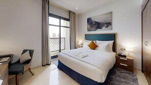 A hotel room with a large bed, a desk with a chair, a window with curtains, and a painting on the wall.