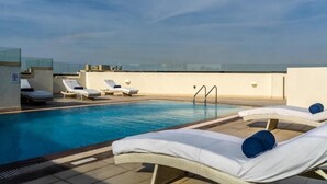 A rooftop pool area with lounge chairs and a clear view of the city skyline.