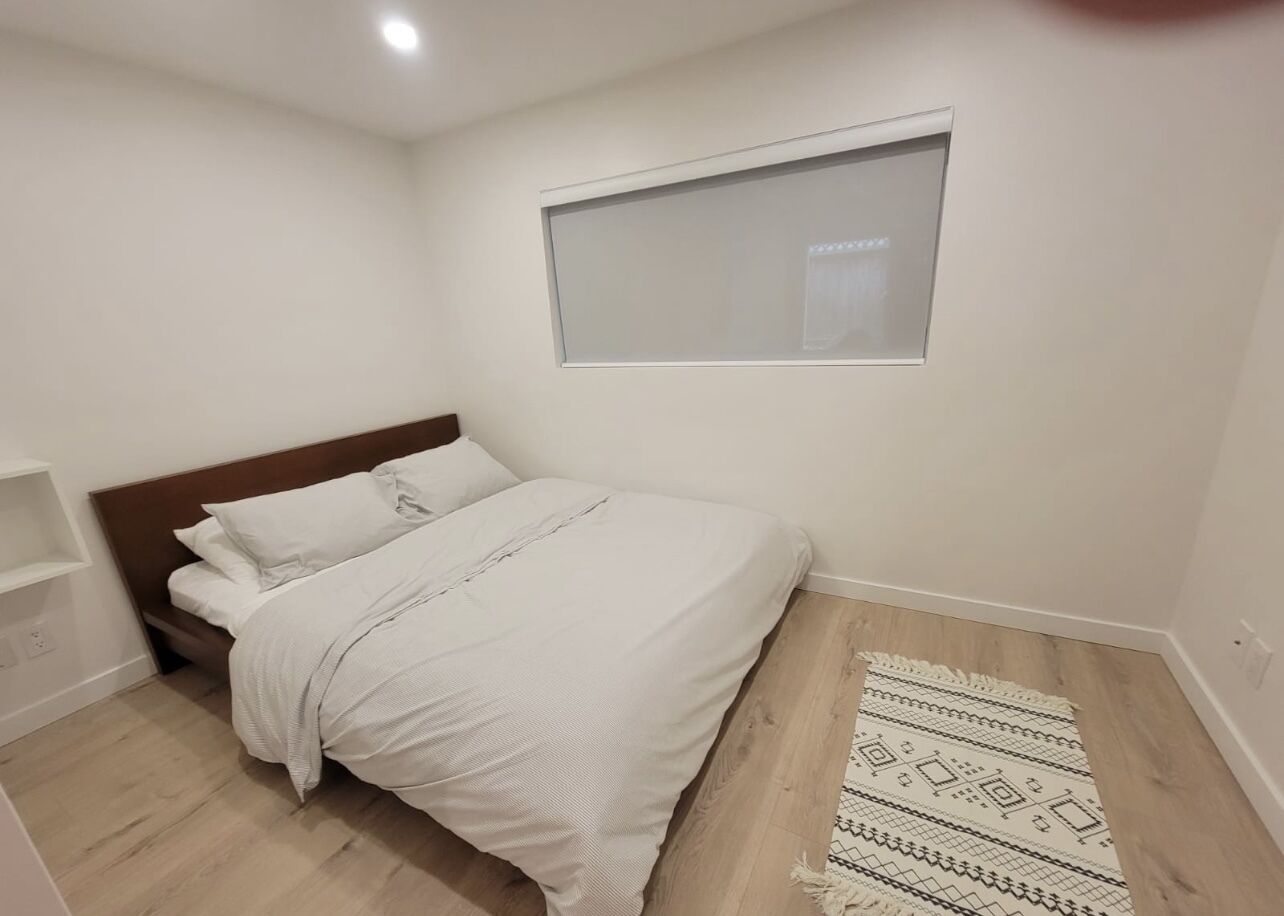 Un dormitorio con una cama, una ventana, piso de madera y una alfombra estampada.