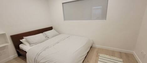 Un dormitorio con una cama, una ventana, piso de madera y una alfombra estampada.