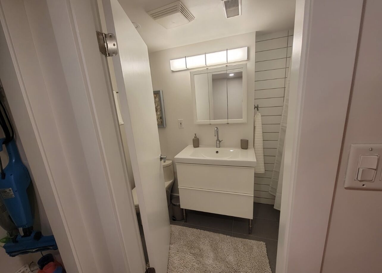 Un baño con lavamanos, espejo e iluminación blanca.
